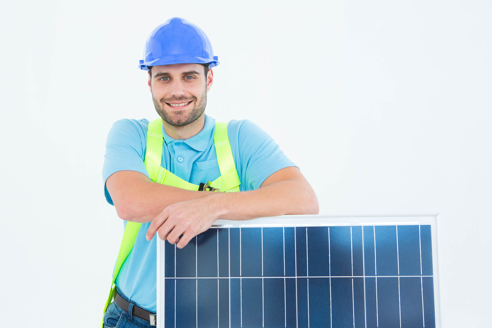 Portrait of happy construction worker leaning on solar panel against white background